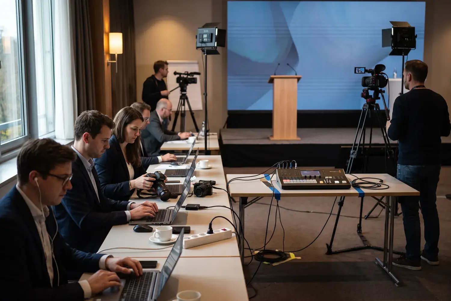 Pressebereich bei einer Pressekonferenz: Journalistinnen und Journalisten an Laptops, daneben Kameras und die Bühne